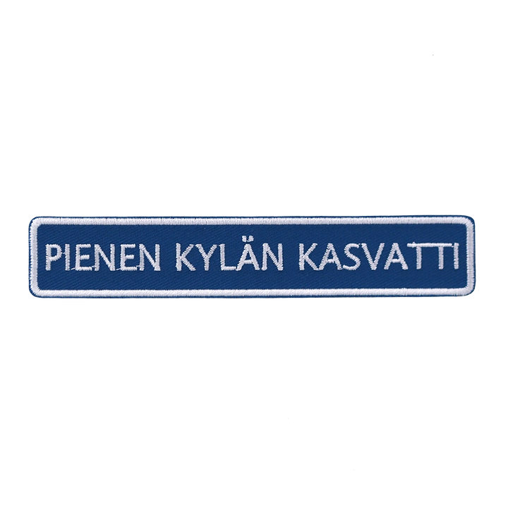 Brodeerattu haalarimerkki, tiekyltti, teksti: Pienen kylän kasvatti.