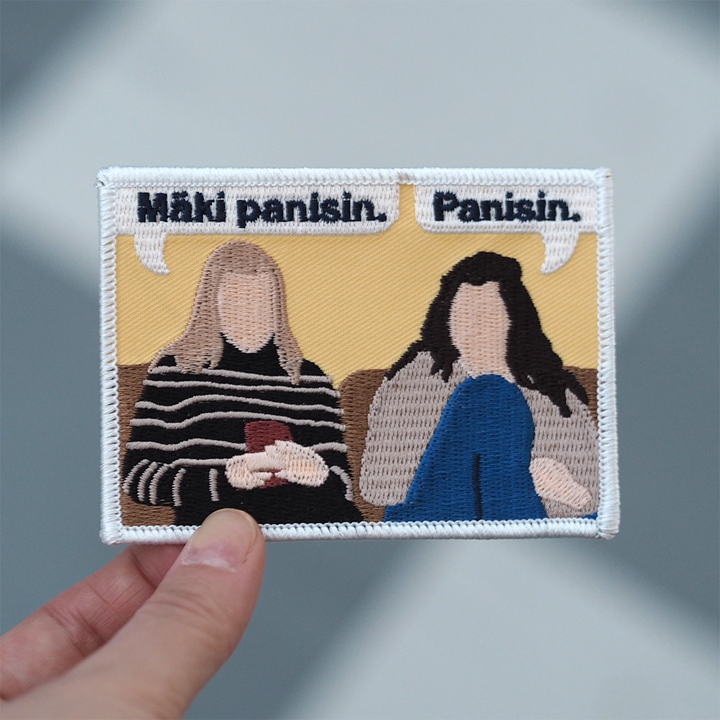 Brodeerattu haalarimerkki, kumman kaa, teksti: Panisin. Mäki panisin. Merkki henkilön kädessä.