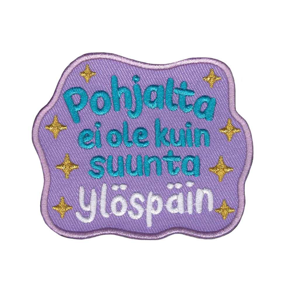 Brodeerattu kangasmerkki, teksti: Pohjalta ei ole kuin suunta ylöspäin.