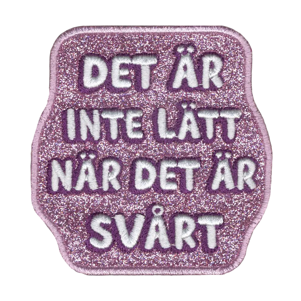 Brodeerattu kangasmerkki, pinkki glitterkangas, teksti: Det är inte lätt när det är svårt.