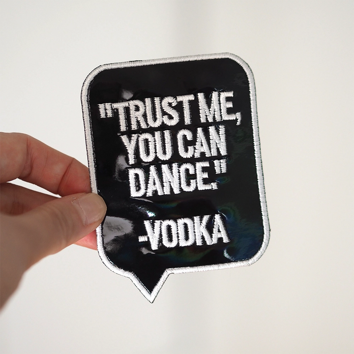 Brodeerattu hologrammihaalarimerkki, musta, teksti: Trust me, you can dance -Vodka. Merkki henkilön kädessä.